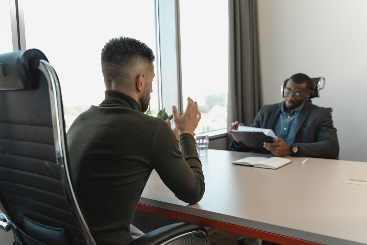 Two men in a job interview setting in a modern office with large windows. global talent finder